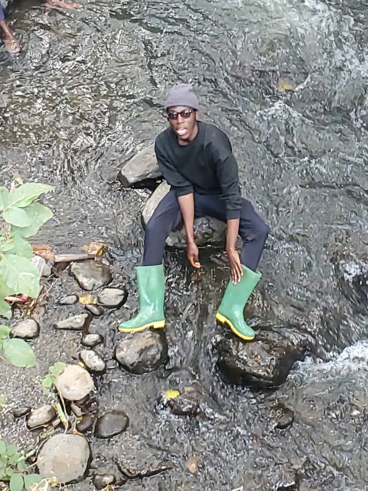 Junior sitting on rocks in a stream wearing green boots.
